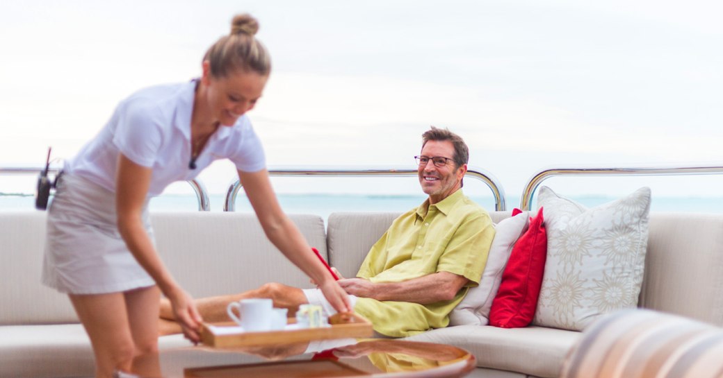 male charter guest is served coffee by a crew member in an outdoor seating area on board motor yacht Remember When