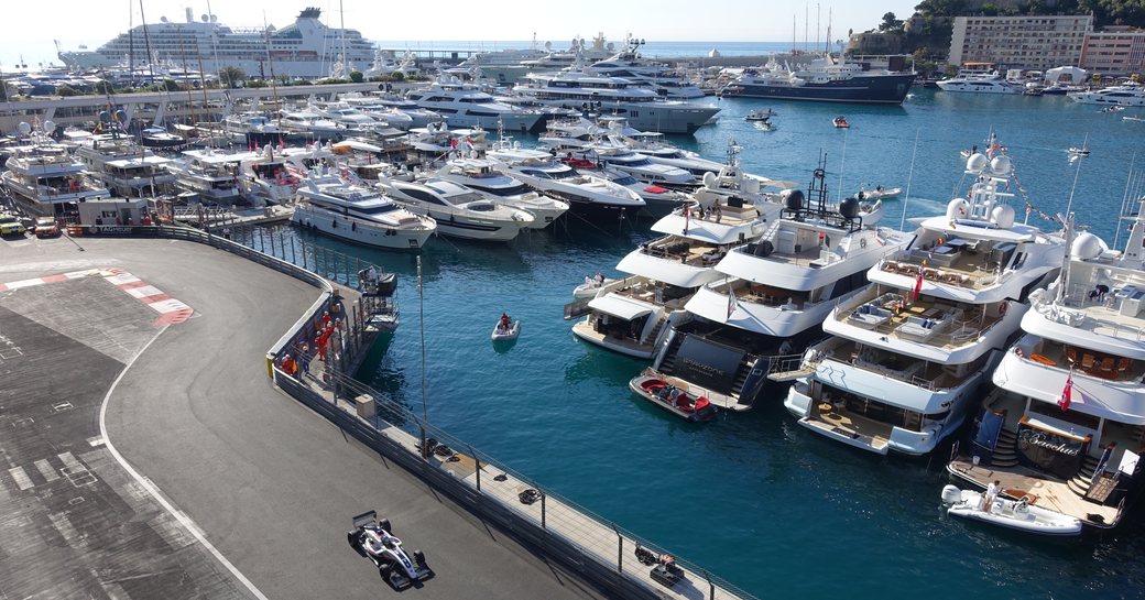 Charter yachts lining up next to racing circuit as car speeds around the track at Formula 1 Monaco Grand Prix