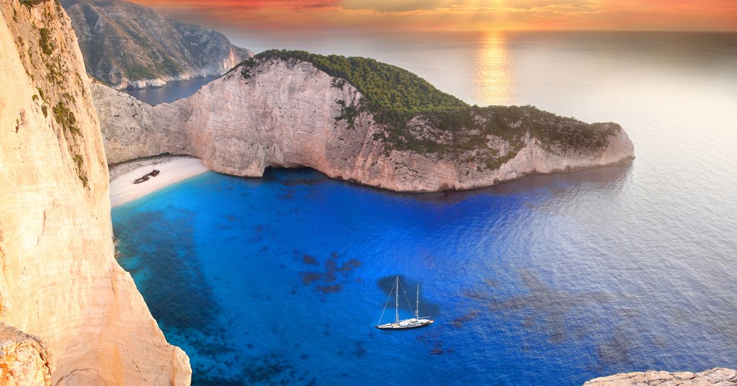 sailing yacht anchors in waters off Navagio beach as the sun sets