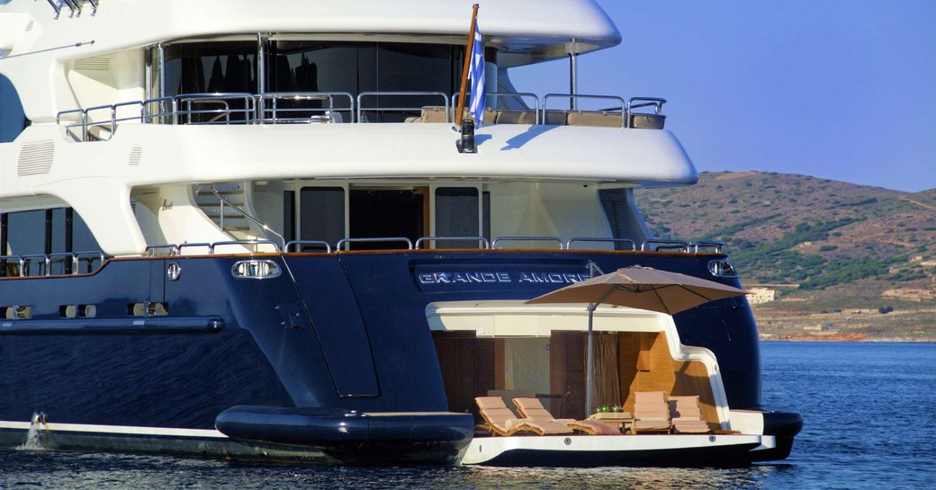 Aft view of charter yacht GRANDE AMORE at sea, with sunloungers and a parasol positioned on the swim platform.