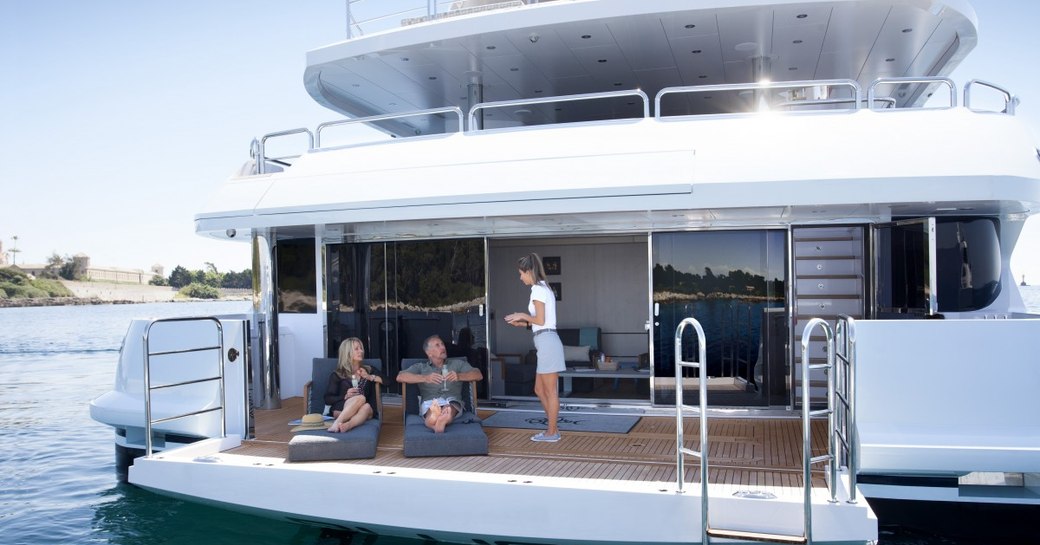 guests lounge on sunpads while crew member serves drinks on the beach club of superyacht ARADOS