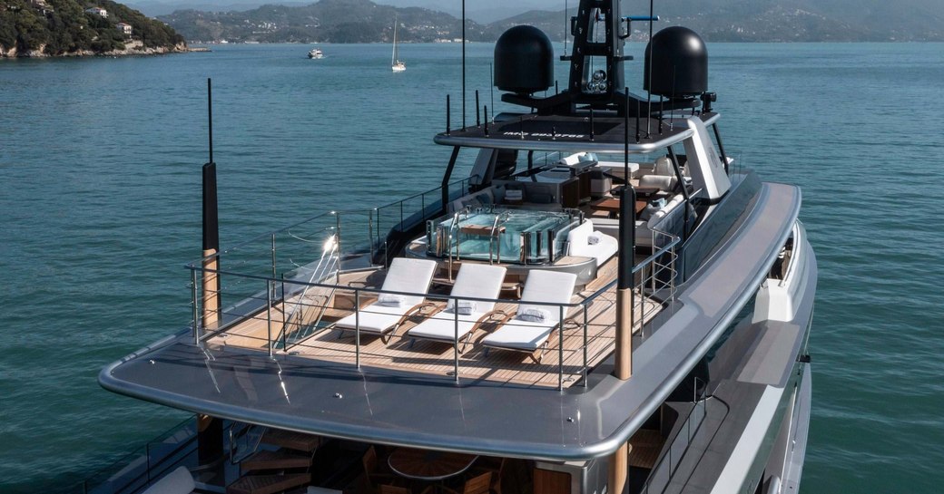 Overview of the sun deck onboard chater yacht ENTERPRISE. Three sun loungers in the foreground with a Jacuzzi behind.