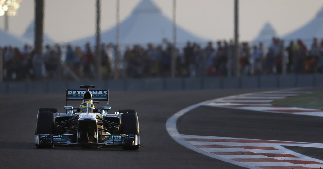 Racer in action on Abu Dhabi Grand Prix track, dusk falling with floodlights on in background.