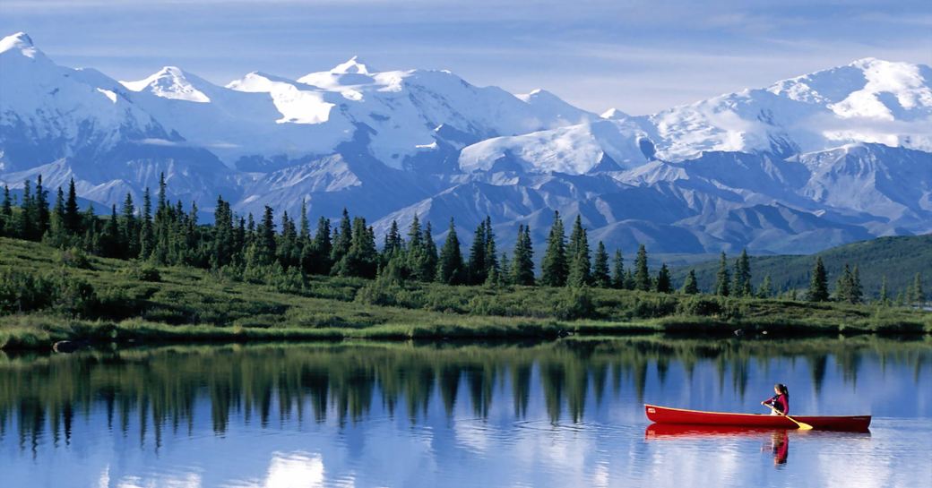 canoeing in Alaska against backdrop of evergreen forests and snow-capped mountains