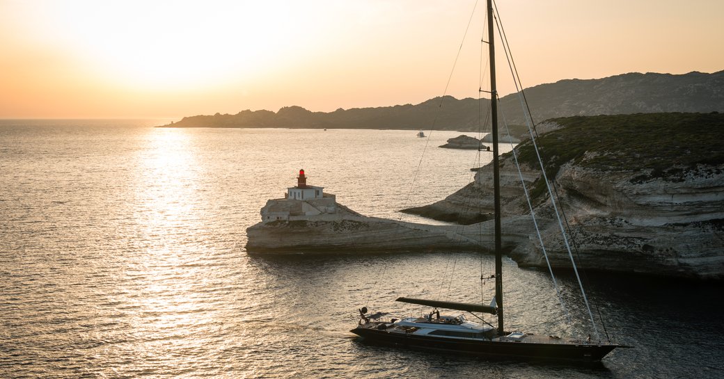 Sailing yacht with lighthouse Madonetta near Bonifacio city at dusk, Corsica island, France