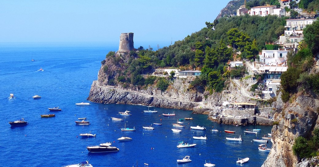 Yachts on clear sea in harbour with hills and houses on them in the foreground