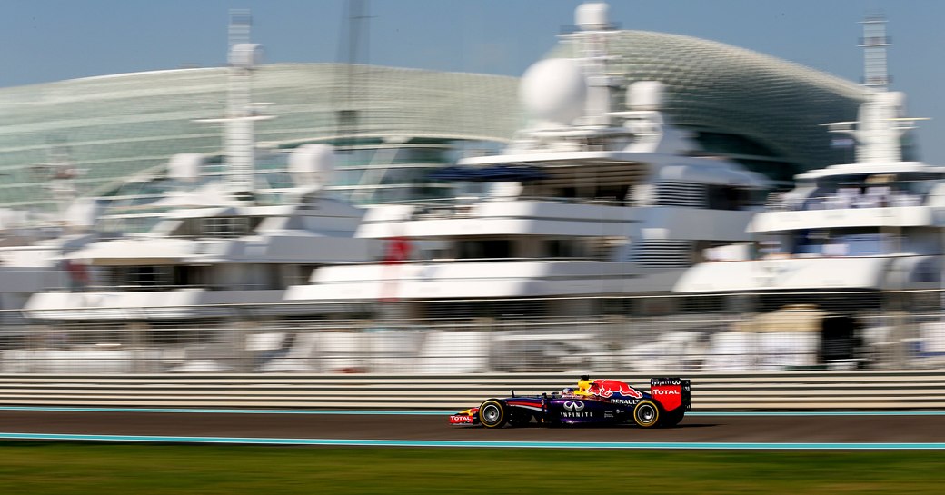 Car on racetrack going past superyachts at Yas Marina Racing Circuit