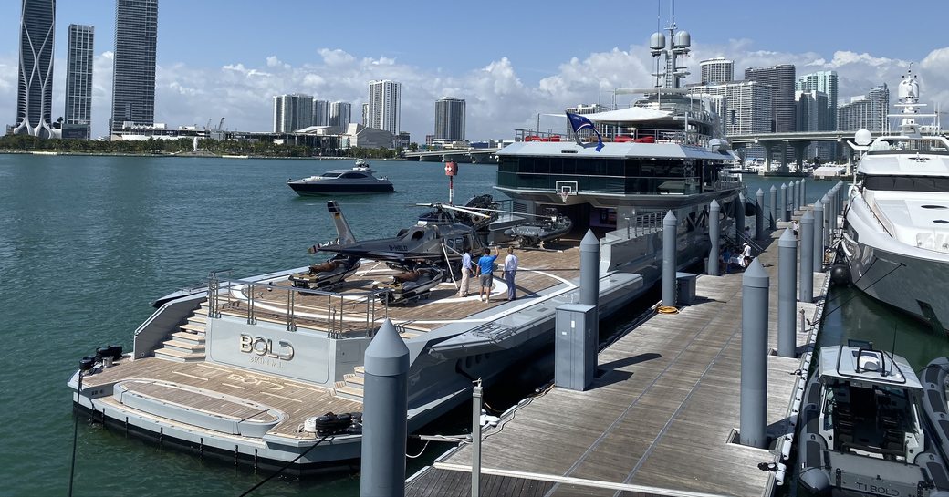 superyacht BOLD in the miami yacht show showcasing her spacious aft deck with ehlipad and helicopter as a group of men perpare for the 2020 miami yacht show