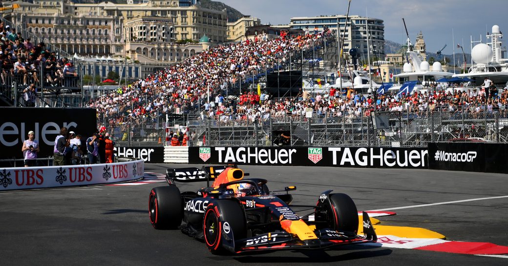 Overview of a Formula One race car in action on the Circuit de Monaco, with full stands in the background