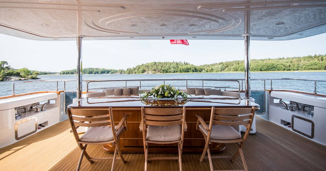 Covered dining area on deck of Superyacht Queen of Sheba with forested coast in background