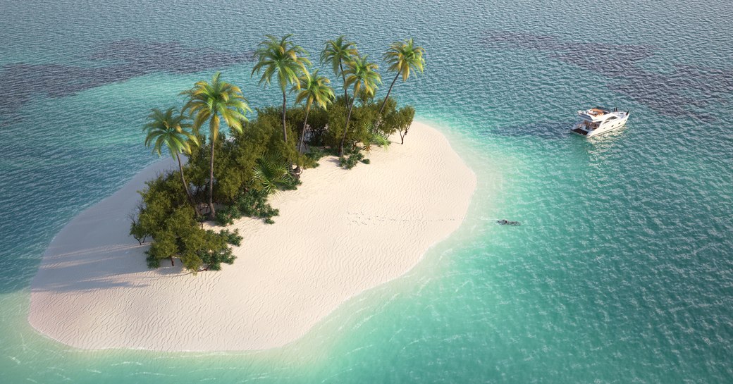 Remote Caribbean island with palms surrounded by clear teal waters and a yacht anchored by the shore