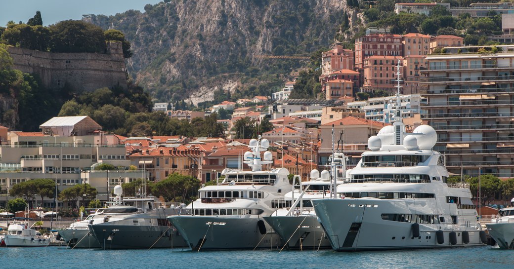 Frontal view of superyachts moored at Monaco Yacht Show in Port Hercules. Monte Carlo visible in background.