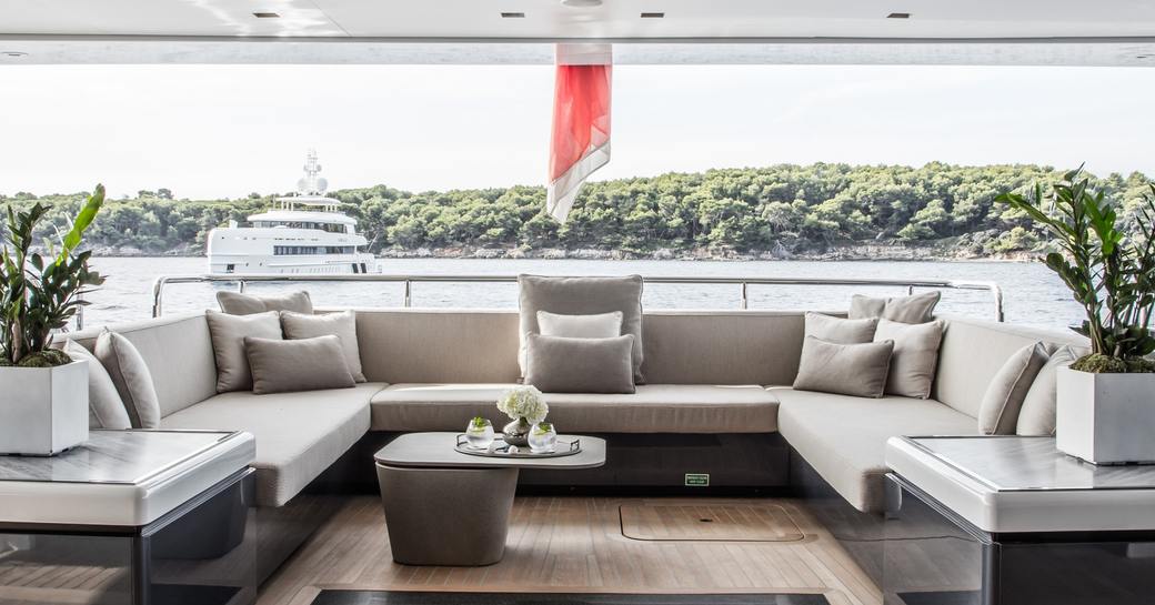 Large comfortable seating area on outside deck of superyacht SEVERIN'S with coastline and another yacht in background