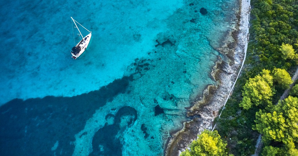 a yacht anchored by a quiet cove with evergreen trees in the middle of summer where guests are enjoying their self isolating yacht charter vacation 