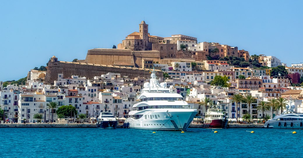 Sea-level view of the old town in Ibiza with a super yacht charter at anchor in the foreground
