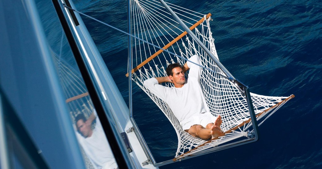 a guest staying aboard charter yacht HARLE relaxes in a hammock over the water