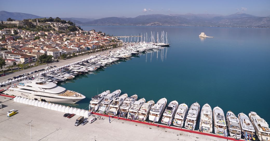 Superyachts line up in Nafplion during the Mediterranean Yacht Show, with the sea in the distance.