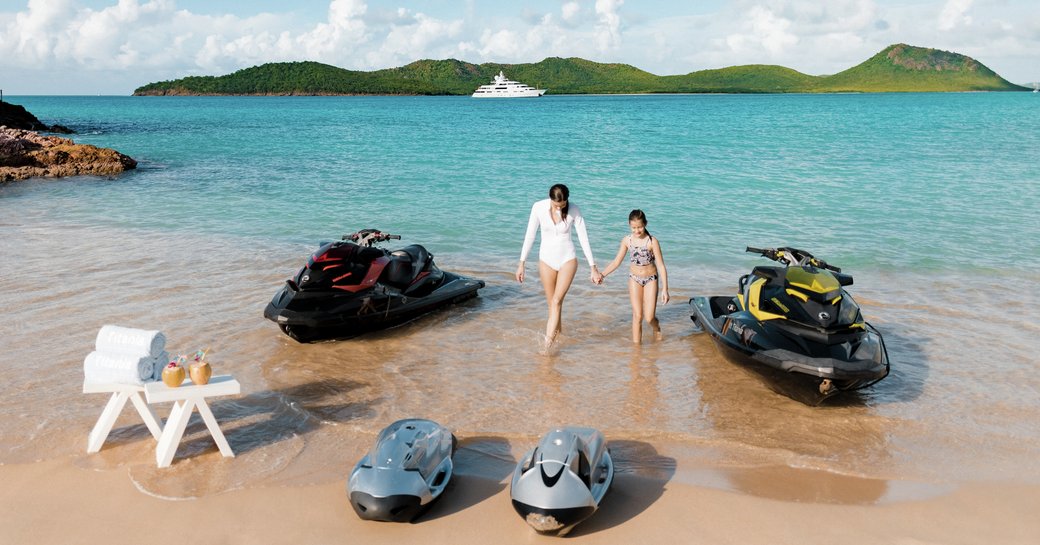 A couple with jet skis ashore with view of MY Titania