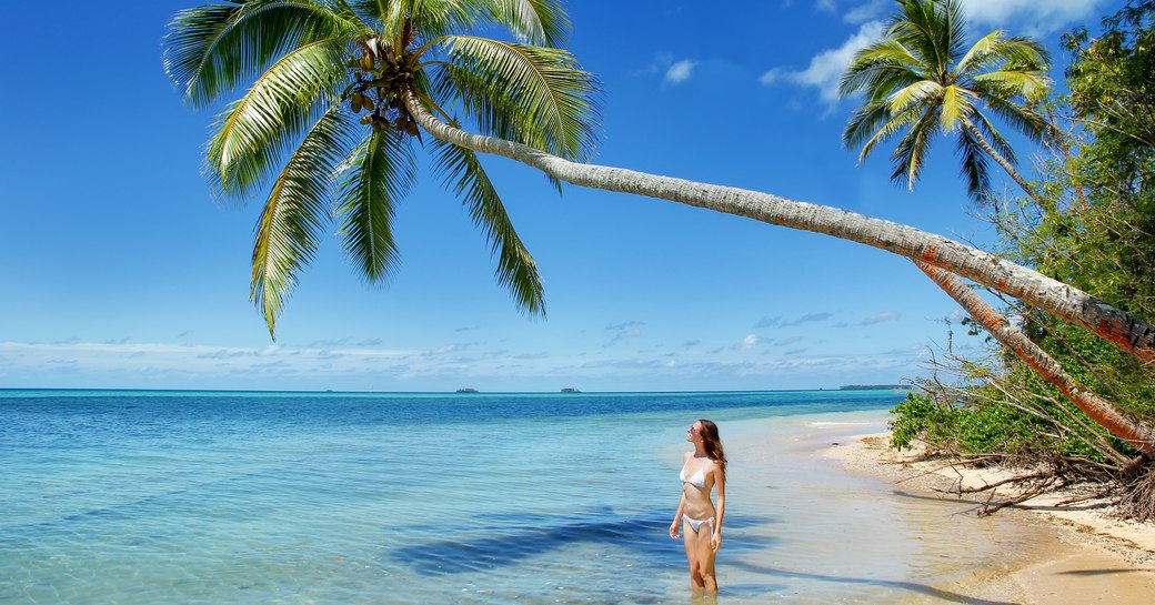 woman stands under a leaning palm tree on beach on Makaha'a island near Tongatapu island in Tonga