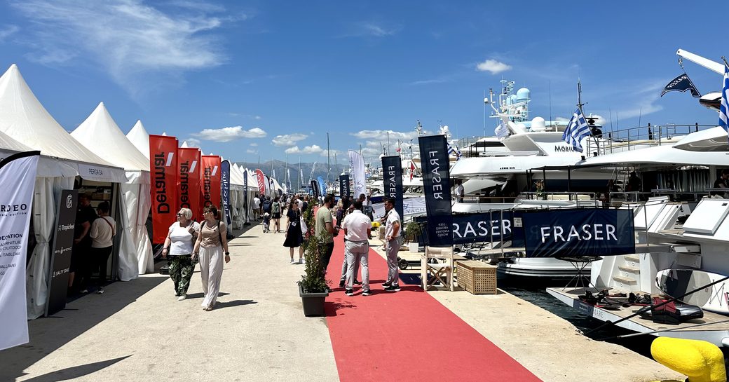 Line of exhibitor tents at the Mediterranean Yacht Show (MEDYS), adjacent to a line of berthed luxury charter yachts