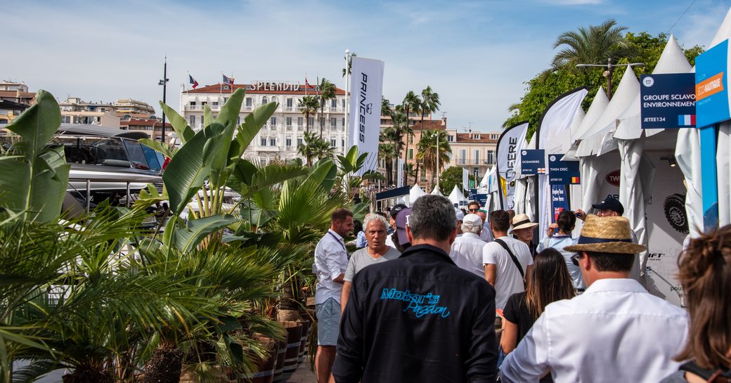 Visitors walking along the dock at the Cannes Yachting Festival, viewing exhibitor tents on the right hand side.