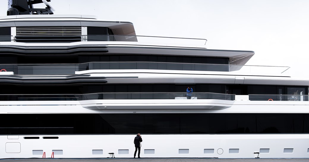 Dock level view of Feadship Project 1011 being transported from construction shed, with a solo onlooker watching the action.