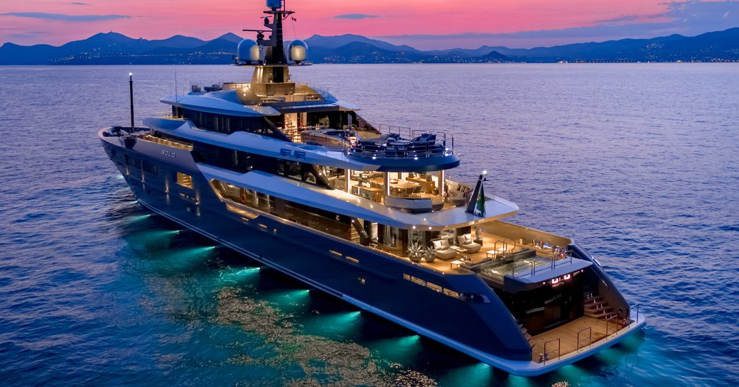 Superyacht SOLO at anchor at night, with green underwater lights and pink sky in background