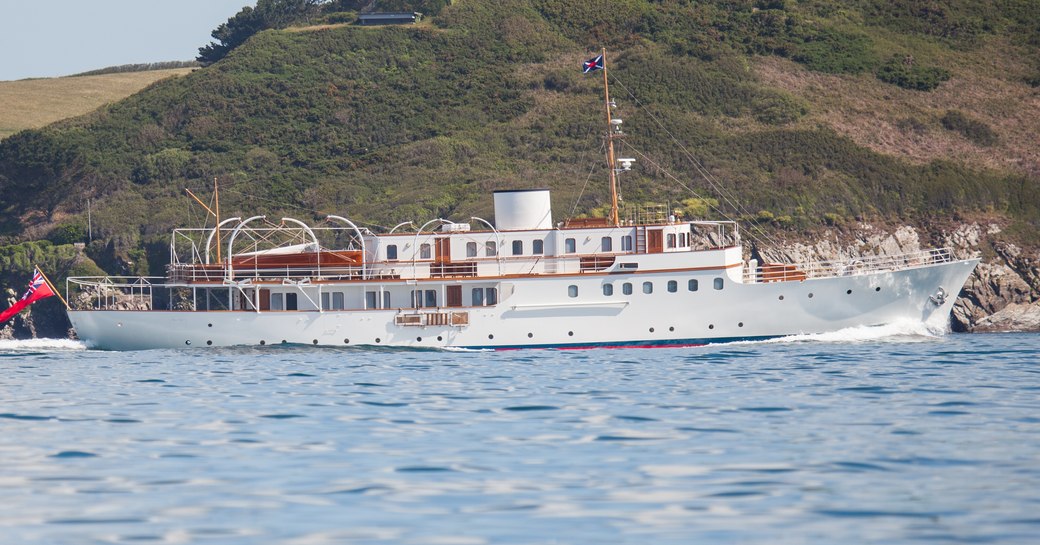 The starboard profile of superyacht MALAHNE with a green hill in the background