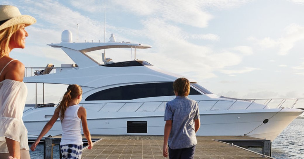 A woman and two children approach a superyacht at the end of a pier