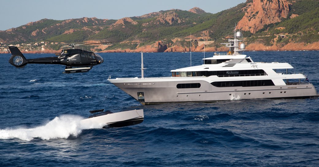 superyacht My Seanna anchors as helicopter prepares to land on helipad and custom tender cruises by