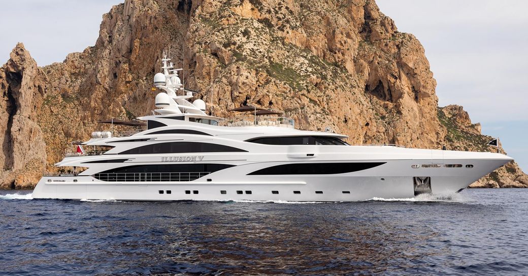 Charter yacht ILLUSION V at sea with rock formation aft