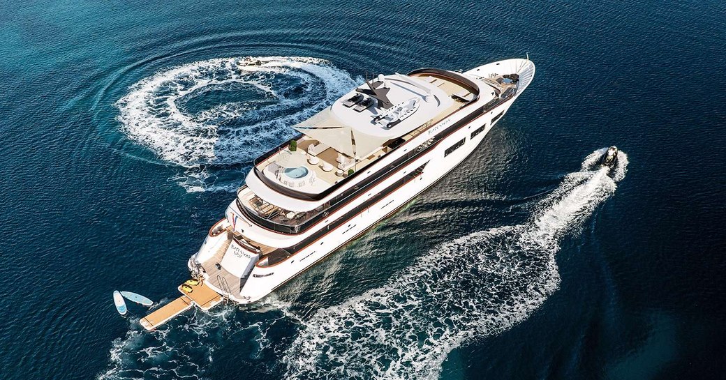 Aerial view looking down on charter yacht BLACK SWAN at sea, with water toys speeding around on either side