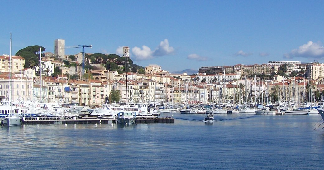 Motor yachts and sailing boats moored in Cannes harbour. Cannes and castle visible in background.