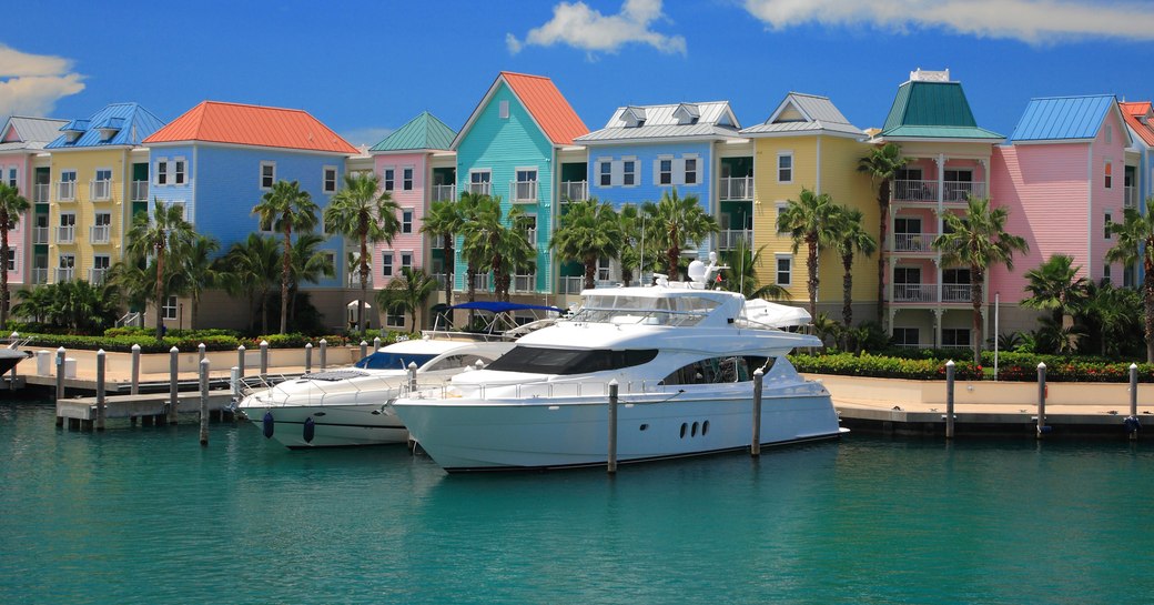 Motor yacht berthed in a marina in the Bahamas, with brightly colored buildings in the background