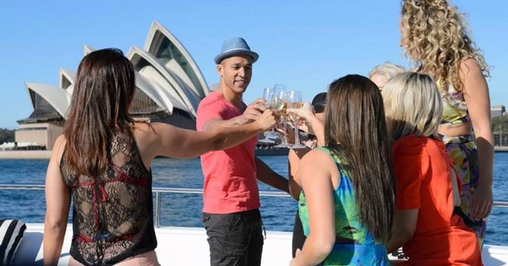 Guests on board a yacht performing a cheers with wine glasses opposite the Sydney Opera House