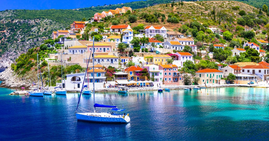 A Grecian coastline with a small settlement by the water and a sailing boat charter in the bay