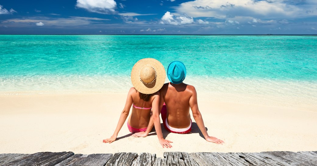 a couple sit on a white sand Maldives beach looking out across the turquoise waters