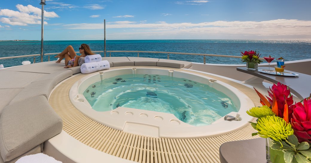 Deck Jacuzzi onboard charter yacht BIG SKY, with bright floral arrangement in the foreground and a female charter guest relaxing in the background