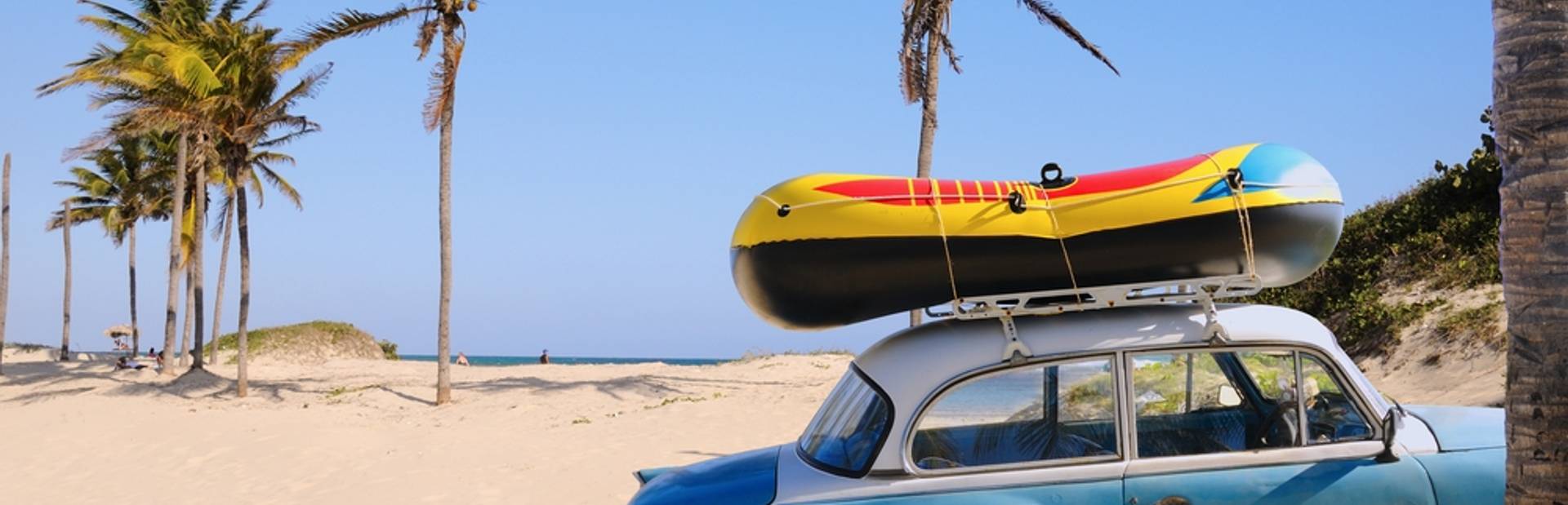 Old blue car with surfboard on the top parked on the beach with palm trees
