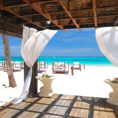 Wooden gazebo with white waving curtains on the beach