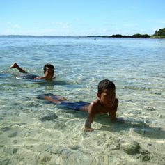 Two children swimming in the sea next to the coast