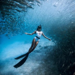 Girl in snorkeling gear surrounded by large school of fish underwater 