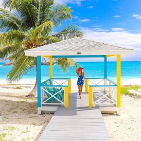Woman standing in brightly colored beach hut by a palm tree