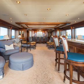 Overview of the main salon onboard charter yacht MISS STEPHANIE, windows stretching along both sides with stools to starboard and blue armchairs to port.