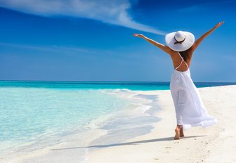 woman dressed in white walks by a Caribbean coast with her arms stretched to the sky in pure serenity while on a luxury yacht charter vacation