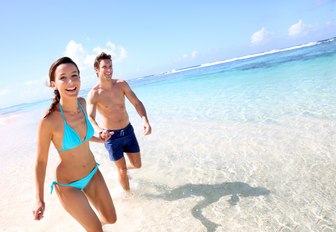 a couple who are on a luxury yacht vacation to the bahamas are running on a beach