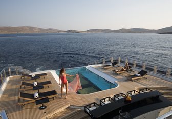 Model prepares for a dip in luxury superyacht Alfa Neros's swimming pool while sailing down exotic ocean looking back onto the island