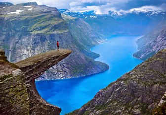 Hiker stands on the edge of Hiker on Trolltunga Rock looking out across the Norwegian Fjords