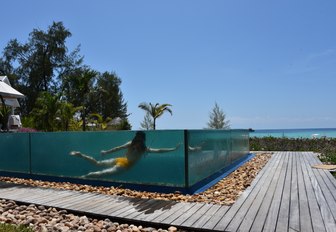 shot of woman underwater through glass of infinity pool on luxury private island, Thanda Island, in East Africa