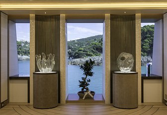 Interiors of superyacht DAR, with windows flanked by glass vases and plant in centre in front of tall winow